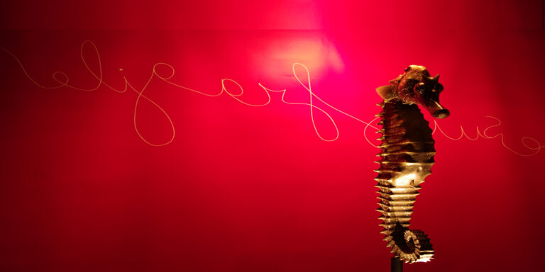Sculpture de hippocampe illuminée sur fond rouge, représentant la beauté du monde marin.