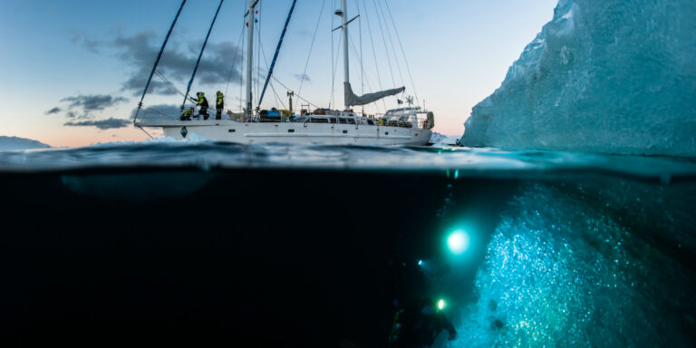 Exploration sous-marine près d'un iceberg avec un voilier et plongeurs équipés.