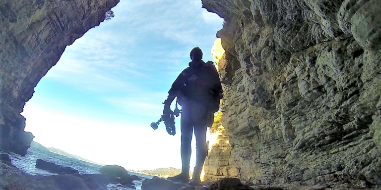 Exploration sous-marine dans une grotte rocheuse avec équipement de plongée et appareil photo.