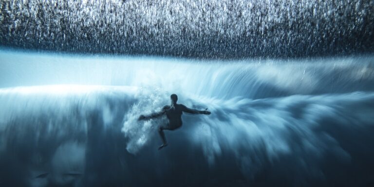 Surfeur plongeant dans une vague majestueuse, explorant les merveilles du monde sous-marin.