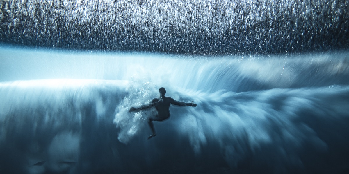 Surfeur plongeant dans une vague majestueuse, explorant les merveilles du monde sous-marin.