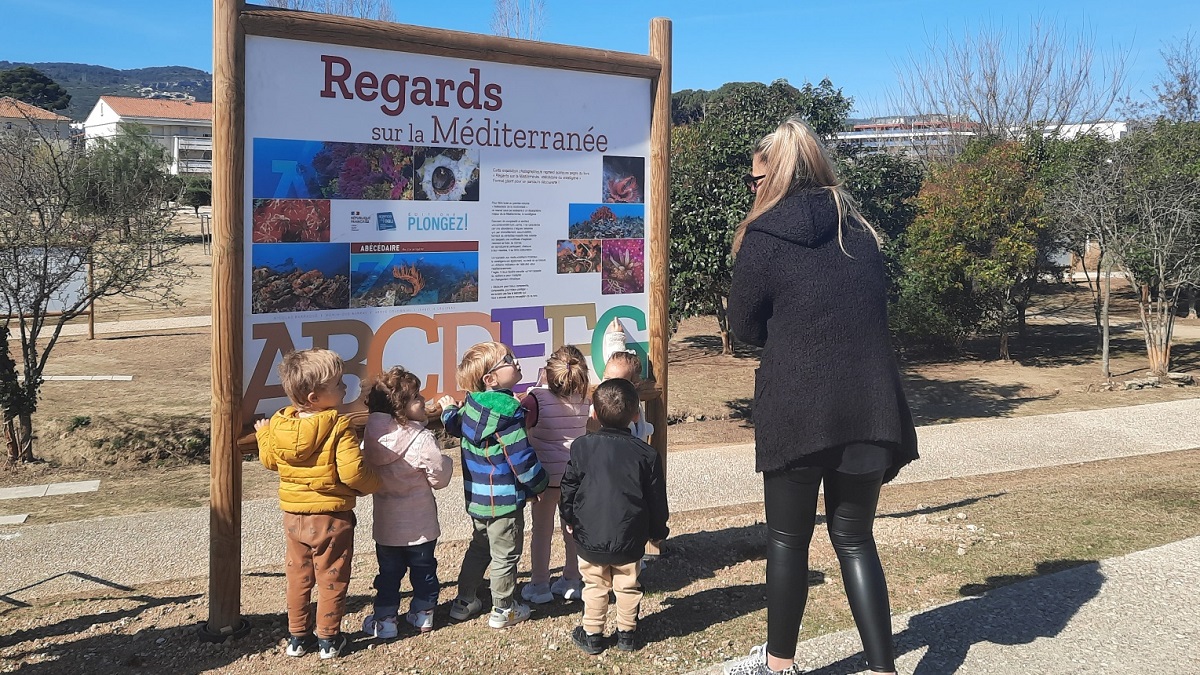 Enfants découvrant le monde marin à travers un panneau éducatif sur la Méditerranée.