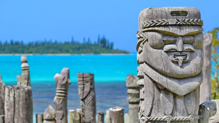 Statues en bois sculptées sur fond de lagon turquoise, symbole de culture océanique.