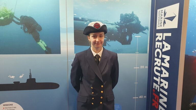 Femme en uniforme naval devant un stand sur les missions sous-marines et la Marine Nationale.