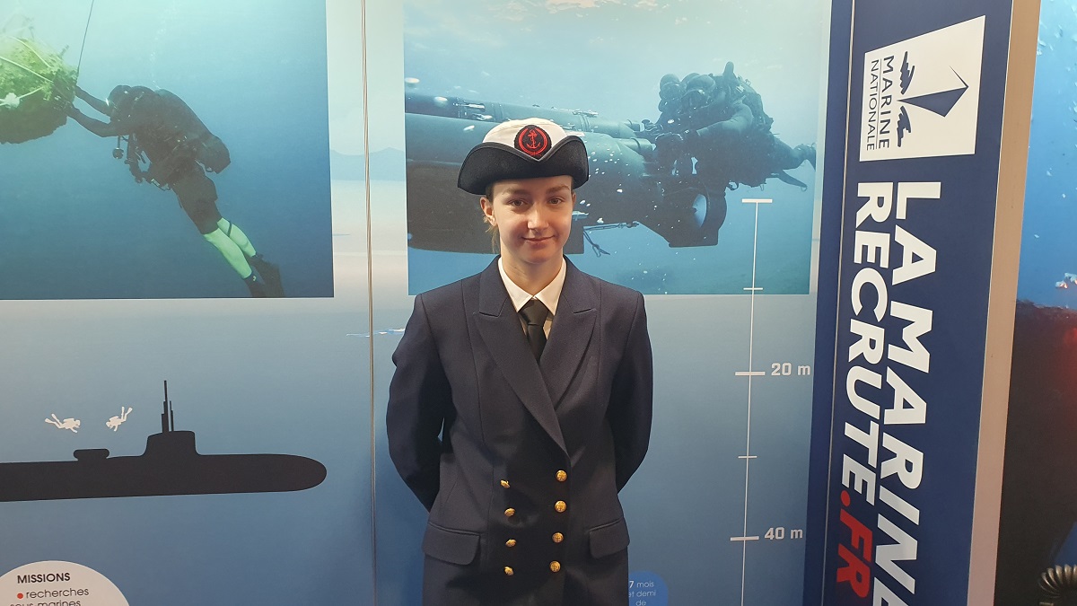 Femme en uniforme naval devant un stand sur les missions sous-marines et la Marine Nationale.