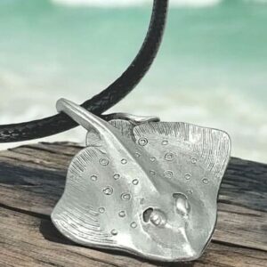 Un pendentif en étain massif représentant une raie pastenague évoque l'élégance marine sur fond de plage exotique. #Océan