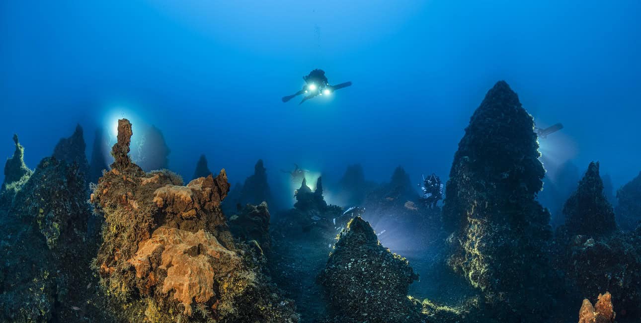Un plongeur explore un paysage sous-marin volcanique illuminé, révélant la beauté mystérieuse des fonds marins. #Exploration