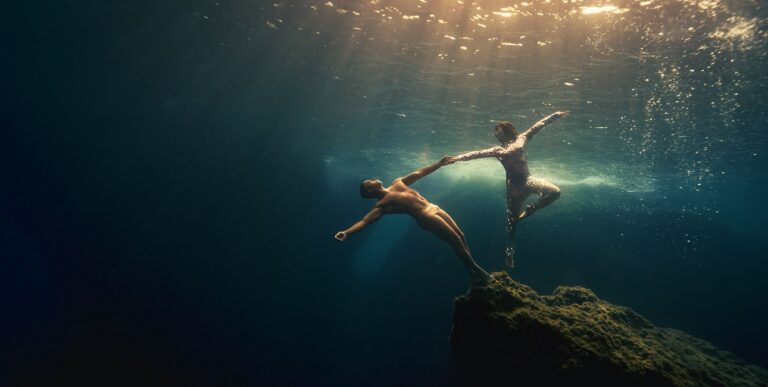 Deux apnéistes exécutent une danse gracieuse sous-marine, illuminée par les rayons du soleil, symbolisant la liberté aquat...