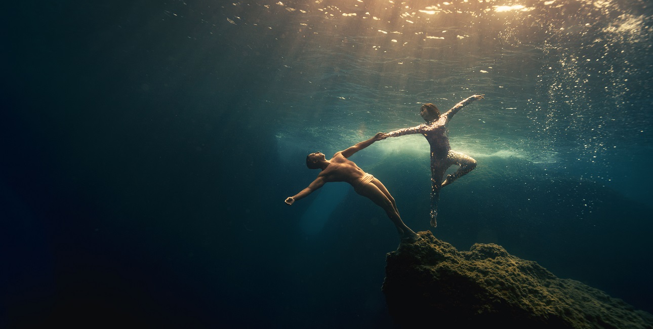 Deux apnéistes exécutent une danse gracieuse sous-marine, illuminée par les rayons du soleil, symbolisant la liberté aquat...