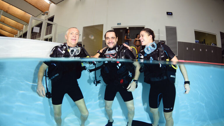 Trois plongeurs souriants s'initient à la plongée sous-marine en piscine, prêts pour une aventure aquatique inoubliable.