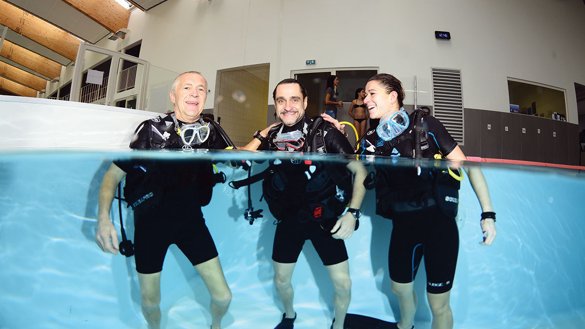 Trois plongeurs souriants s'initient à la plongée sous-marine en piscine, prêts pour une aventure aquatique inoubliable.