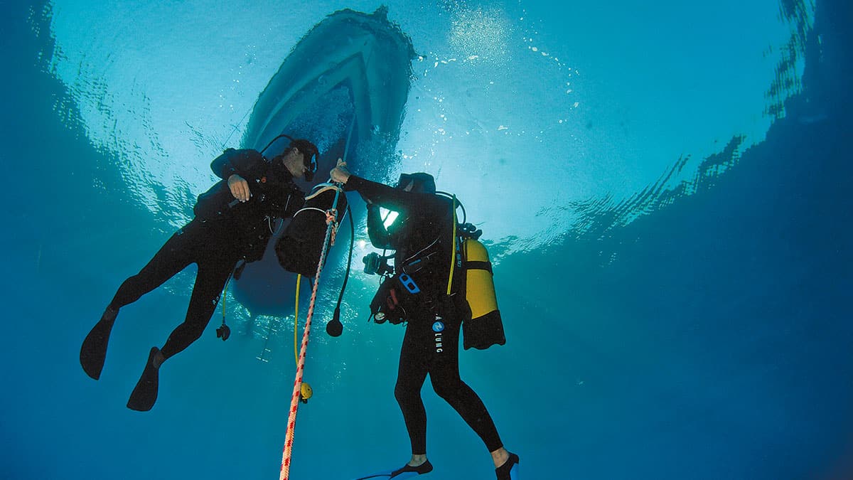 Deux plongeurs échangent sous un bateau, symbolisant l'aventure et la formation en plongée dans un océan cristallin.