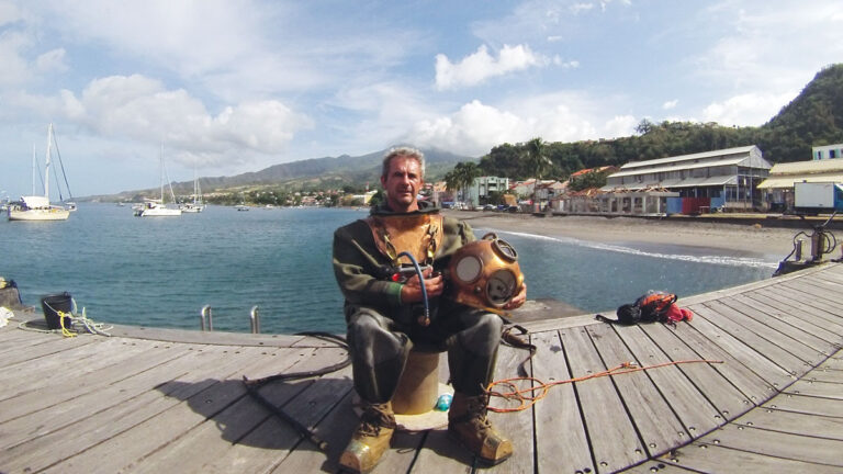 Un plongeur en tenue vintage se prépare à explorer les eaux paisibles d'une baie tropicale, symbole d'aventure sous-marine.