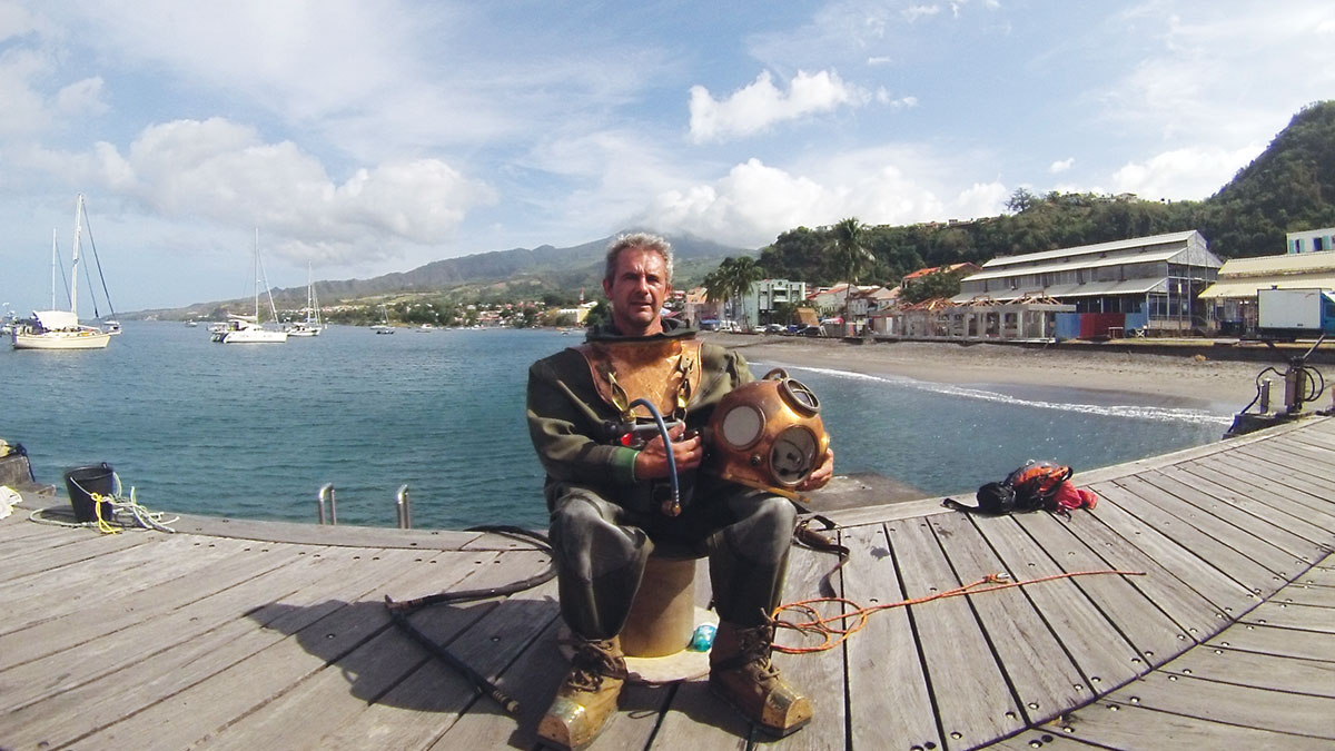 Un plongeur en tenue vintage se prépare à explorer les eaux paisibles d'une baie tropicale, symbole d'aventure sous-marine.