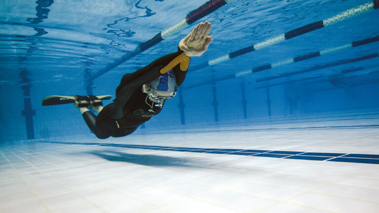 Un apnéiste glisse sous l'eau dans une piscine, illustrant la maîtrise et la sérénité de la plongée en apnée.