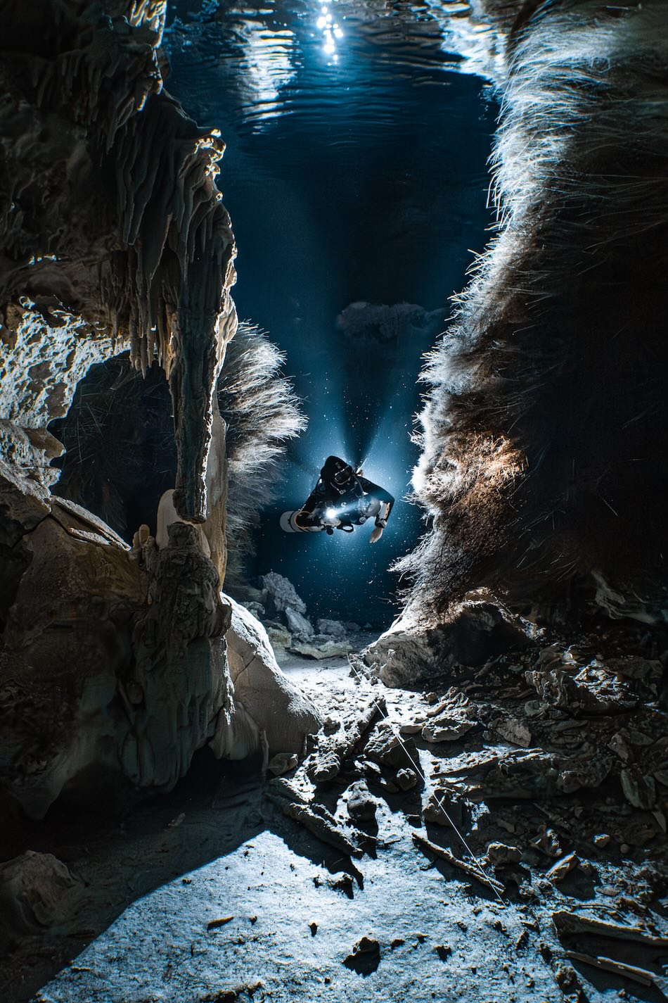 Plongée dans une grotte sous-marine illuminée, révélant des formations spectaculaires et un aventurier explorateur.