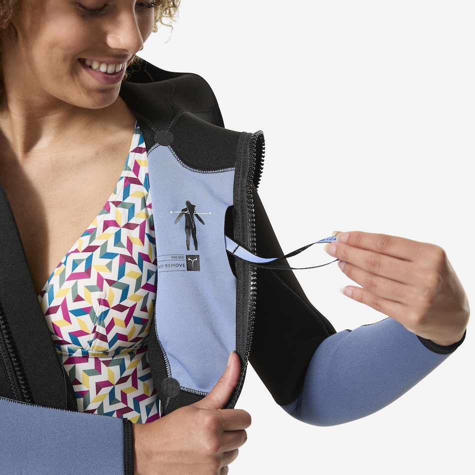 Une femme souriante ajuste sa combinaison de plongée, essentielle pour explorer les merveilles sous-marines.