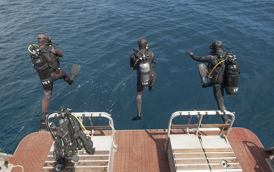 Trois plongeurs s'apprêtent à plonger dans les eaux cristallines, équipés pour l'exploration sous-marine.