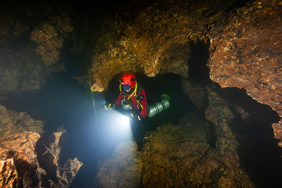 Plongeur explorant une grotte sous-marine avec une lampe, découvrant les merveilles aquatiques.