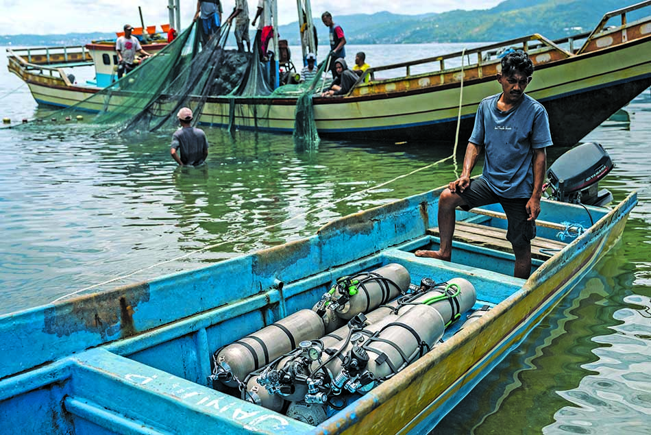 Un plongeur prépare son équipement dans une barque, entouré par des pêcheurs en mer.