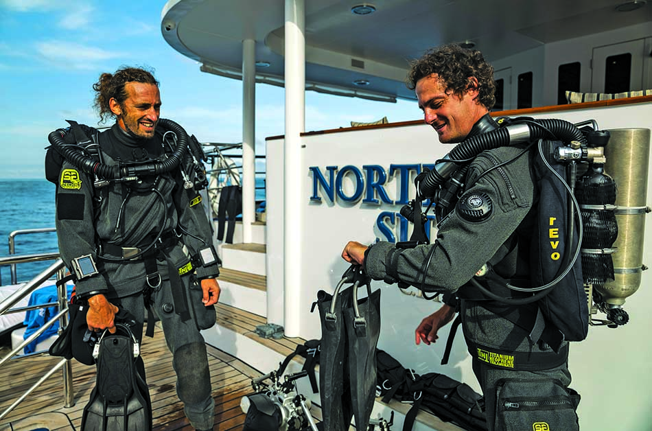Deux plongeurs en scaphandre préparent leur équipement sur un bateau dédié à l'exploration sous-marine.