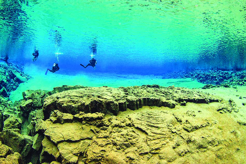Des plongeurs explorent un paysage sous-marin fascinant avec des formations rocheuses et des eaux cristallines.