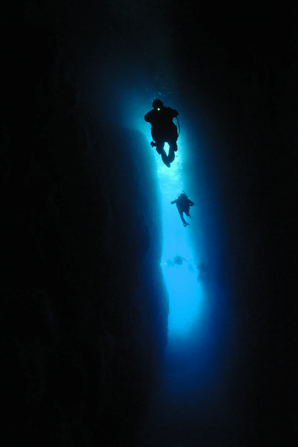 Deux plongeurs explorent une fissure sous-marine illuminée par une lumière bleue apaisante.