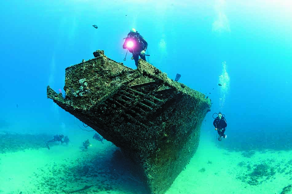Deux plongeurs explorent une épave sous-marine recouverte de coraux, révélant la beauté du monde aquatique.