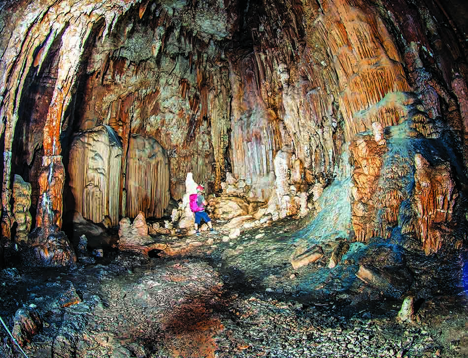 Un plongeur explore une grotte sous-marine ornée de stalactites et stalagmites colorées.