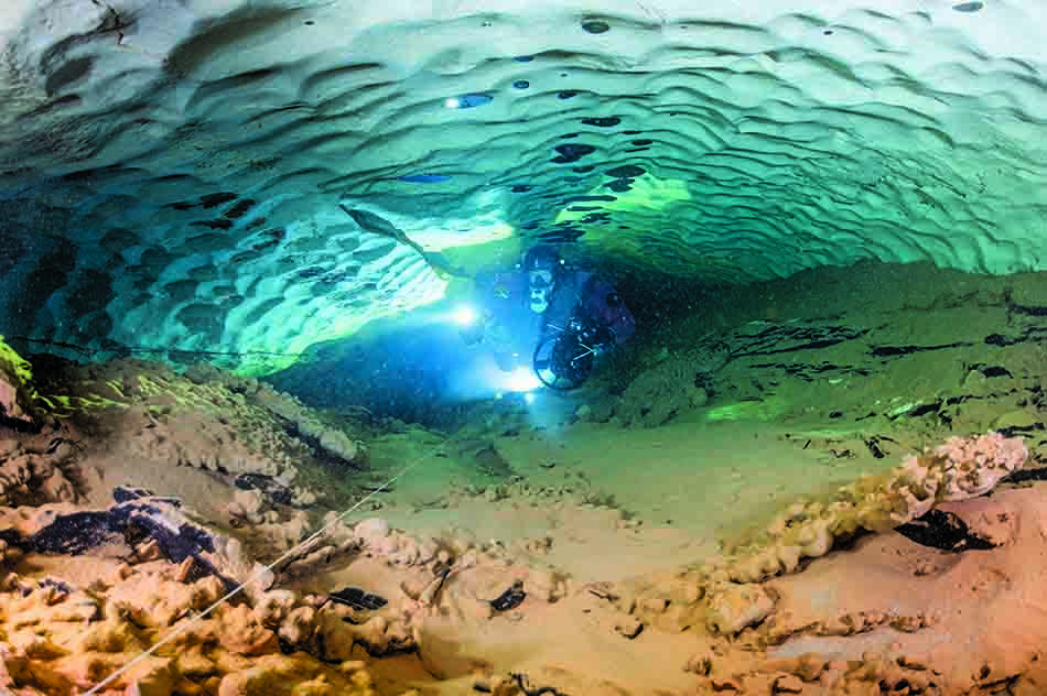 Un plongeur explore un passage sous-marin illuminé, révélant la beauté cachée des fonds marins.