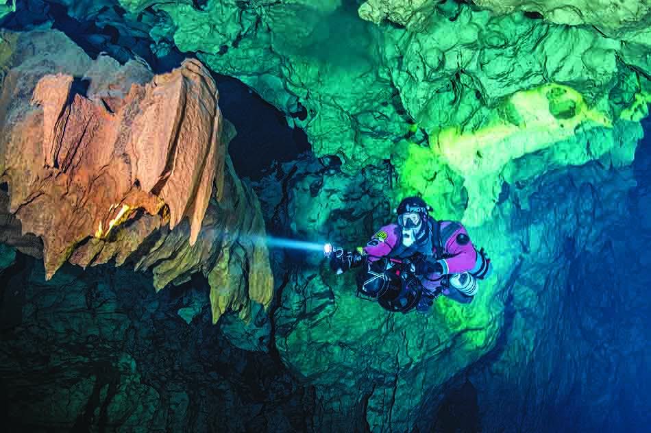 Plongée dans une grotte sous-marine illuminée par des stalactites colorées et des reflets aquatiques.