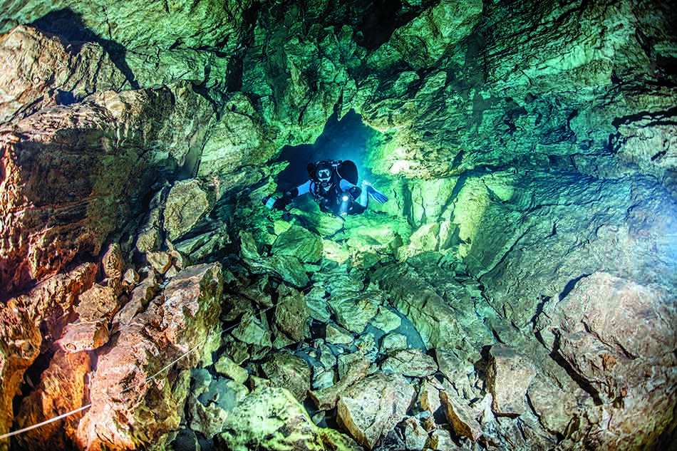 Plongeur explorant une grotte sous-marine, révélant des formations rocheuses fascinantes et une lumière mystérieuse.