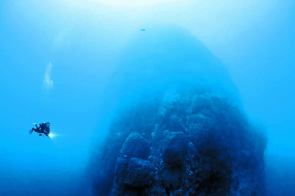 Plongeur explorant une formation rocheuse sous-marine dans un environnement océanique fascinant.